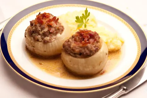 Zwei gefüllte Bamberger Zwiebeln mit Hackfleisch und Speck, serviert mit Kartoffelpüree auf einem Teller mit blau-goldener Bordüre.