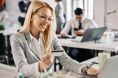 Uśmiechnięta kobieta z kartą płatniczą w ręku, korzystająca z laptopa. To idealne rozwiązanie dla spółki z o.o. do zarządzania finansami.