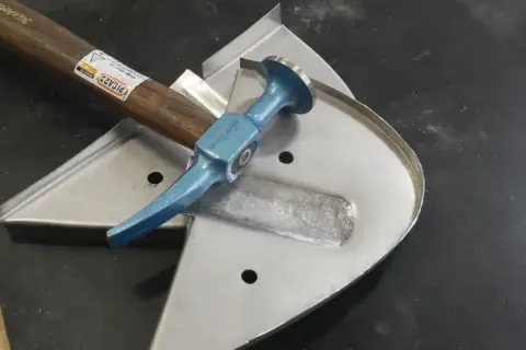 Karosserie Werkzeug für Oldtimer: Ein Ausbeul-Pinnhammer liegt auf einem Blechteil, bereit für die Restaurierung.