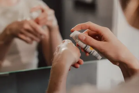 Eine Hand hält eine Flasche mit Vitamin C Booster. Ein Tropfen Serum landet auf der anderen Hand, bereit für die abendliche Hautpflege.