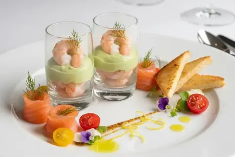 Recette entrée froide gastronomique facile : crevettes et avocat en verrine, saumon fumé roulé, toasts grillés, tomates cerises et fleurs comestibles.