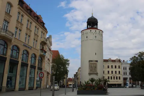 Der Reichenturm dominiert den Marienplatz Görlitz, flankiert von historischen Gebäuden und blühenden Blumenbeeten.
