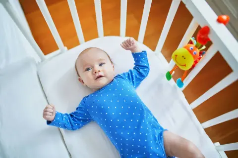 Maluch w niebieskim bodziaku w kropki, leżący w łóżeczku, przeżywa skok rozwojowy 10 tydzień. Z radością podnosi rączki.