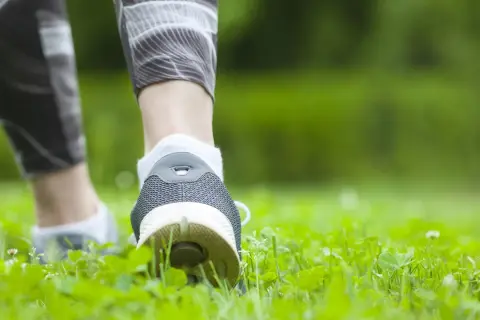 Füße in Sportschuhen und Laufhose bewegen sich durch grünes Gras. Spazieren gehen ist Sport und gut für die Gesundheit.