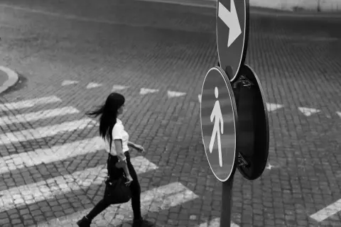 Una donna attraversa la strada su un selciato, seguendo le indicazioni di un segnale pedonale. Fotografia di strada.