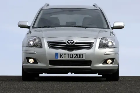 Srebrny Toyota Avensis z włączonymi światłami dziennymi i przeciwmgielnymi, gotowy do podróży.