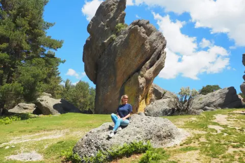 Mujer sentada en roca, con imponente formación rocosa detrás. Un paisaje natural que demuestra que merece la pena visitar Soria.