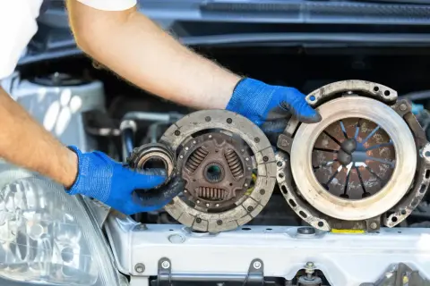 Mechanik w niebieskich rękawiczkach prezentuje części do wymiany sprzęgła: docisk i tarczę.