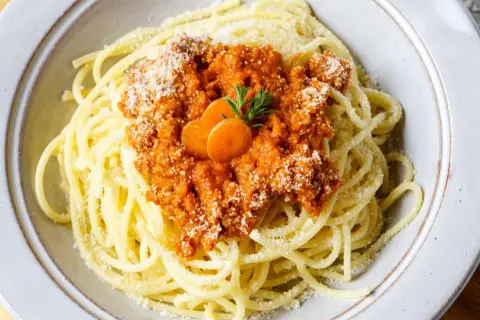 Spaghetti Bolognese, zubereitet im Thermomix, mit Karottenscheiben und Parmesan bestreut.