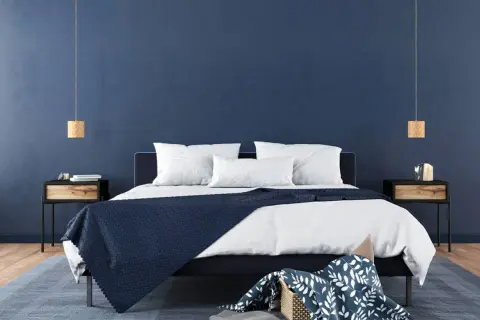 Ein modernes Schlafzimmer mit tiefblauen Wänden, die Ruhe und Harmonie ausstrahlen – eine ideale feng shui schlafzimmer farbe. Weiße Bettwäsche und dunkle Akzente schaffen ein stilvolles Ambiente.