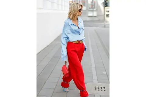 Donna con pantaloni rossi ampi e camicia azzurra, borsa rossa e sandali blu. Un look audace per scoprire come abbinare pantaloni rossi con stile.