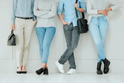 Cztery osoby w stonowanych kolorach, prezentujące styl normcore. Jasne jeansy, beżowe spodnie i szare dżinsy tworzą bazę dla prostych, wygodnych stylizacji.