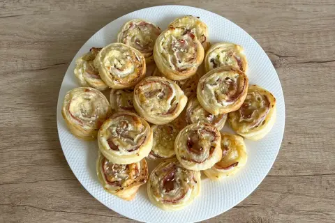 Talerz pełen chrupiących ślimaków z ciasta francuskiego z szynką i serem, posypanych sezamem. Idealna przekąska na imprezę.