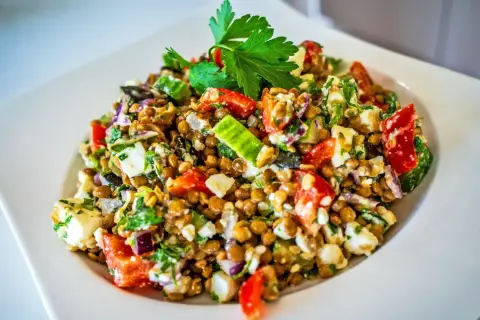 Ein bunter Linsensalat mit Feta, Tomaten, Gurken und frischer Petersilie, garniert mit einem Petersilienblatt.