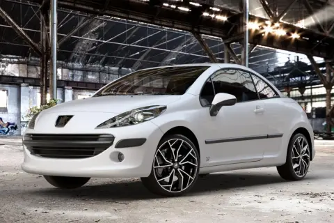 Vit Peugeot 207 cabriolet med snygga fälgar i en övergiven lagerlokal. Inga problem här, bara stil!