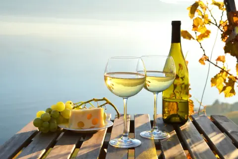Dwa kieliszki białego wina, butelka, winogrona i ser na drewnianym stole. Idealne na wieczór, gdy liczymy wino białe kcal.