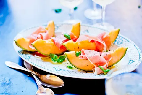 En vacker tallrik med melon och skinka, garnerad med basilika och peppar. Perfekt för en lätt och elegant förrätt.