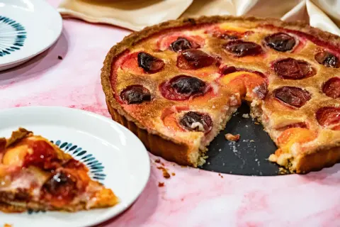 Une délicieuse tarte aux prunes rouges, garnie de poudre d'amande, est prête à être dégustée. Une part a déjà été servie.