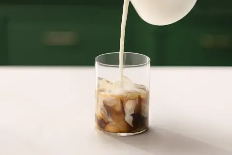 Mjölk hälls i ett glas med is och kaffe. Perfekt för ett enkelt iskaffe recept.