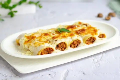 Canelones de carne gratinados, cubiertos con bechamel y queso derretido, listos para disfrutar.