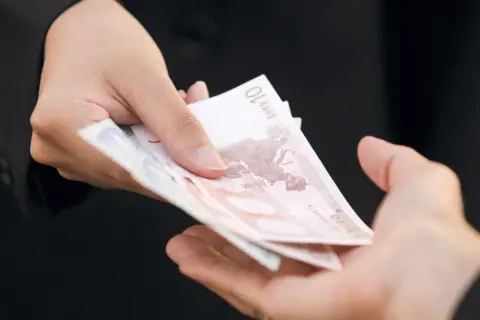 Dwie dłonie przekazują sobie banknoty euro. Zastanawiasz się, ile kosztuje windykacja należności?