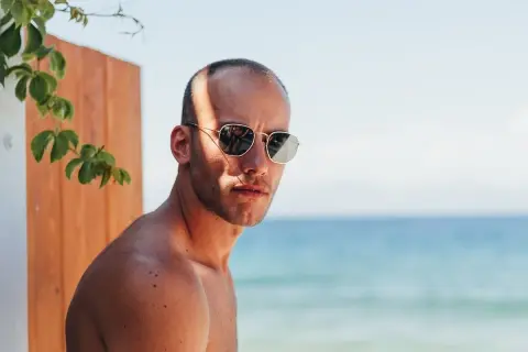 Uomo con capelli cortissimi, occhiali da sole e sfondo mare.
