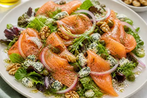 Salade colorée avec saumon fumé, fromage bleu émietté, noix, câpres et oignons rouges sur un lit de verdure.