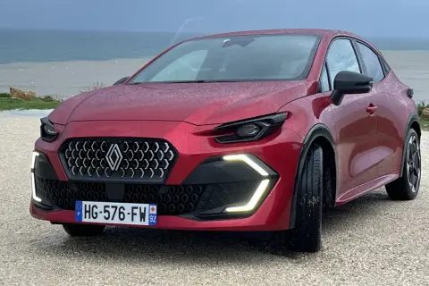 Nowe Clio 2026 w kolorze czerwonym, z nowoczesnym grillem i światłami LED, zaparkowane nad morzem.