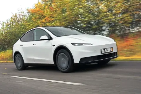 Biały Tesla Y w ruchu, otoczony rozmazanymi jesiennymi drzewami. Czy warto kupić?