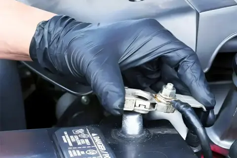 Ręka w czarnej rękawiczce dokręca śrubę na klemie akumulatora samochodowego.