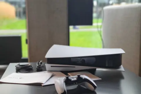 Konsola PlayStation 5 z kontrolerem i kablami na czarnym stole.