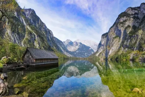 Holzhütte am Königssee, ein Juwel in Bayern, spiegelt sich im klaren Wasser vor majestätischen Bergen.