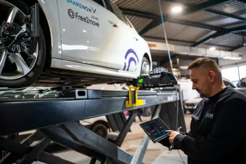 Mechaniker prüft mit Tablet die Achsvermessung an einem Auto. Die Spur verstellt, wird hier präzise eingestellt.