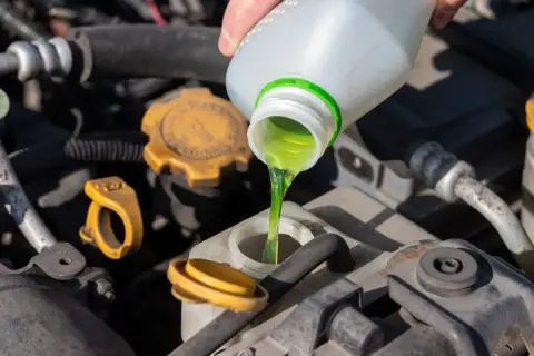 Vertiendo líquido verde brillante, que es el anticongelante, en el motor de un coche.