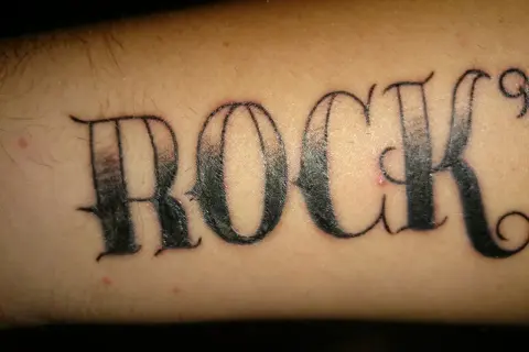 Ein Pickel stört das "ROCK"-Tattoo auf dem Arm.