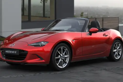Czerwone Mazda MX-5, jedne z najbardziej pożądanych aut sportowych, lśni na tle nowoczesnej architektury.