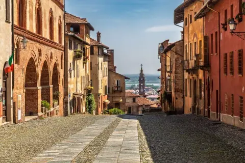 Rue pavée bordée de maisons colorées, avec une église au loin. Un charmant village du Piémont, Italie.