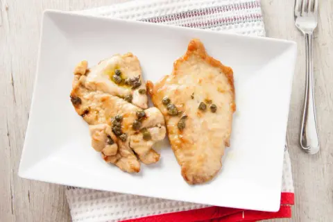 Due fette di fesa di tacchino con capperi su un piatto bianco. Un pasto leggero, ideale per chi cerca fesa di tacchino calorie.
