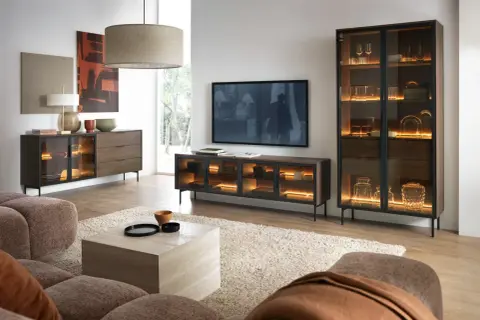Modernes Wohnzimmer mit gemütlicher Couch. Ein Sideboard und Vitrinenschrank in grau und braun kombinieren, beleuchtet mit warmem Licht.