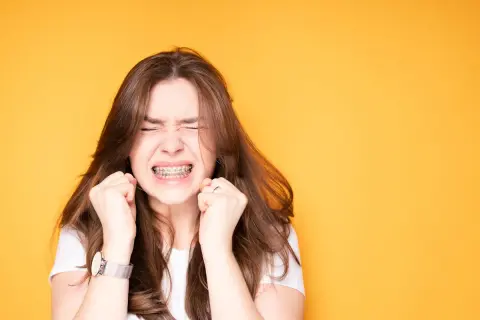Ragazza con apparecchio ai denti, espressione di sforzo, mani strette. Un'immagine che evoca il percorso delle labbra prima e dopo apparecchio.