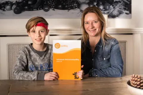 Moeder en zoon houden een oefenboek spelling vast. Vind je het leuk om te leren spellen?
