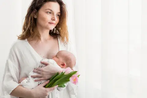 Mama tuli z dzieckiem na rękach, trzymając bukiet różowych tulipanów. To piękny obrazek z 4 trymestru.