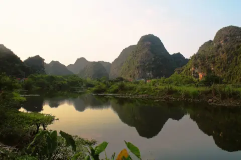 Krajobraz Ninh Binh z odbijającymi się w wodzie wapiennymi górami porośniętymi zielenią.
