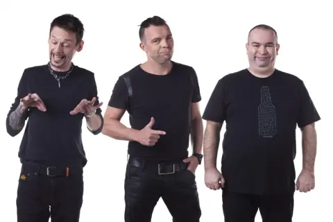 Trzech członków kabaretu Ani Mru Mru w czarnych strojach, każdy z innym wyrazem twarzy i gestem.