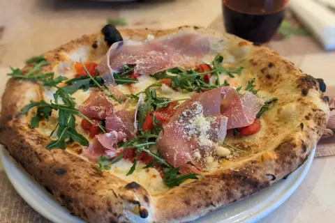 Eine köstliche Pizza mit Prosciutto, Rucola und Tomaten, die aussieht wie die beste Pizza Neapels.