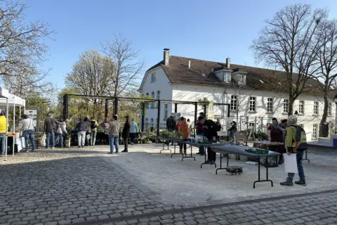 Menschen besuchen einen Markt mit Pflanzen und Ständen vor einem weißen Gebäude. Ein schönes Beispiel für Veranstaltungen in Bergisch Gladbach.