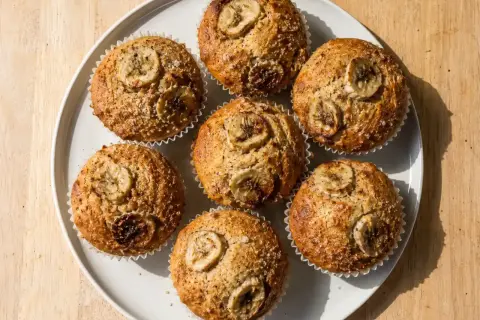 Sju gyllene bananmuffins med skivor av banan på toppen, serverade på en vit tallrik. Perfekt för fika!
