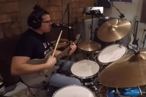 Muzyk w słuchawkach gra na gitarze i perkusji, jakby wpadł w **rush tom sawyer**.