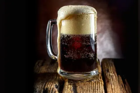 Boccale di birra scura con schiuma abbondante, forse la birra americana più famosa, su un tavolo di legno rustico.