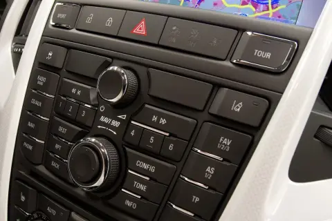 Panel środkowy z nawigacją i przyciskami w Astrze J. Widoczne pokrętła, przyciski radia, telefonu i nawigacji.
